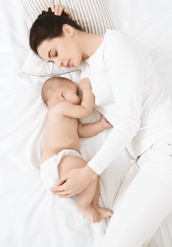 Mother and sleeping baby resting peacefully on bed at home