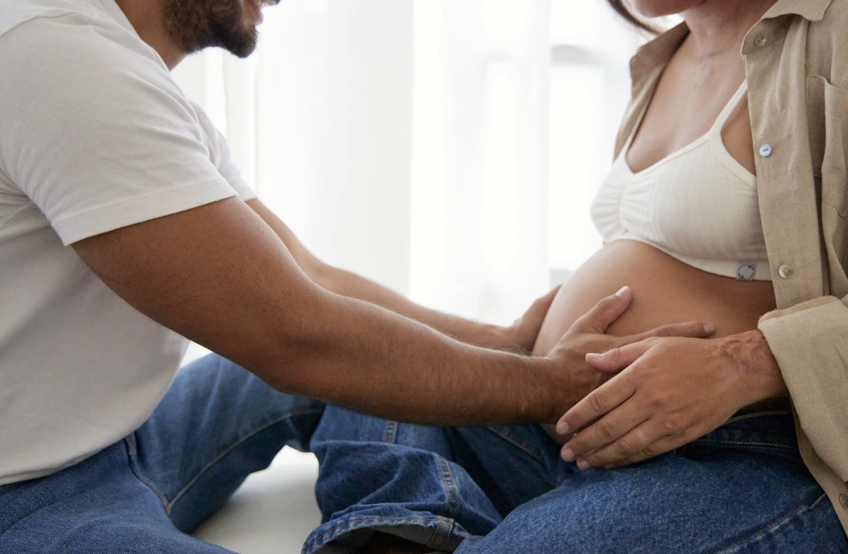 Couple's hands together on pregnant belly, warm natural light