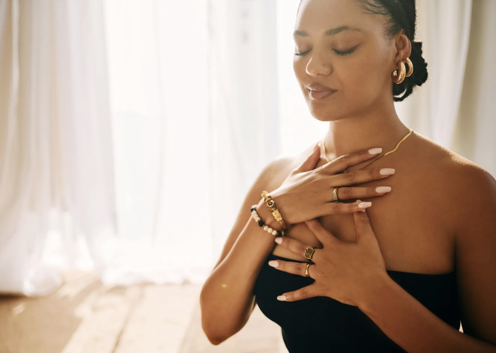 Pregnant woman with hands on chest, eyes closed, breathing calmly in soft natural light