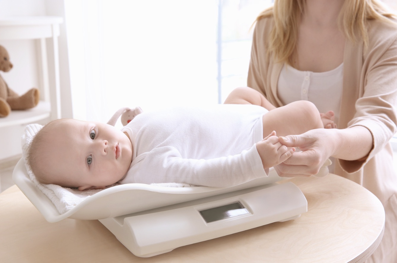 Baby being weighed on a baby scale, mother holding baby's hand