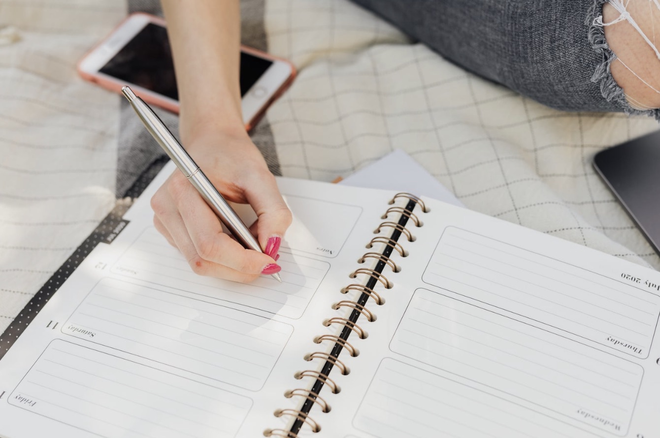 Hand writing in a weekly planner notebook on soft surface