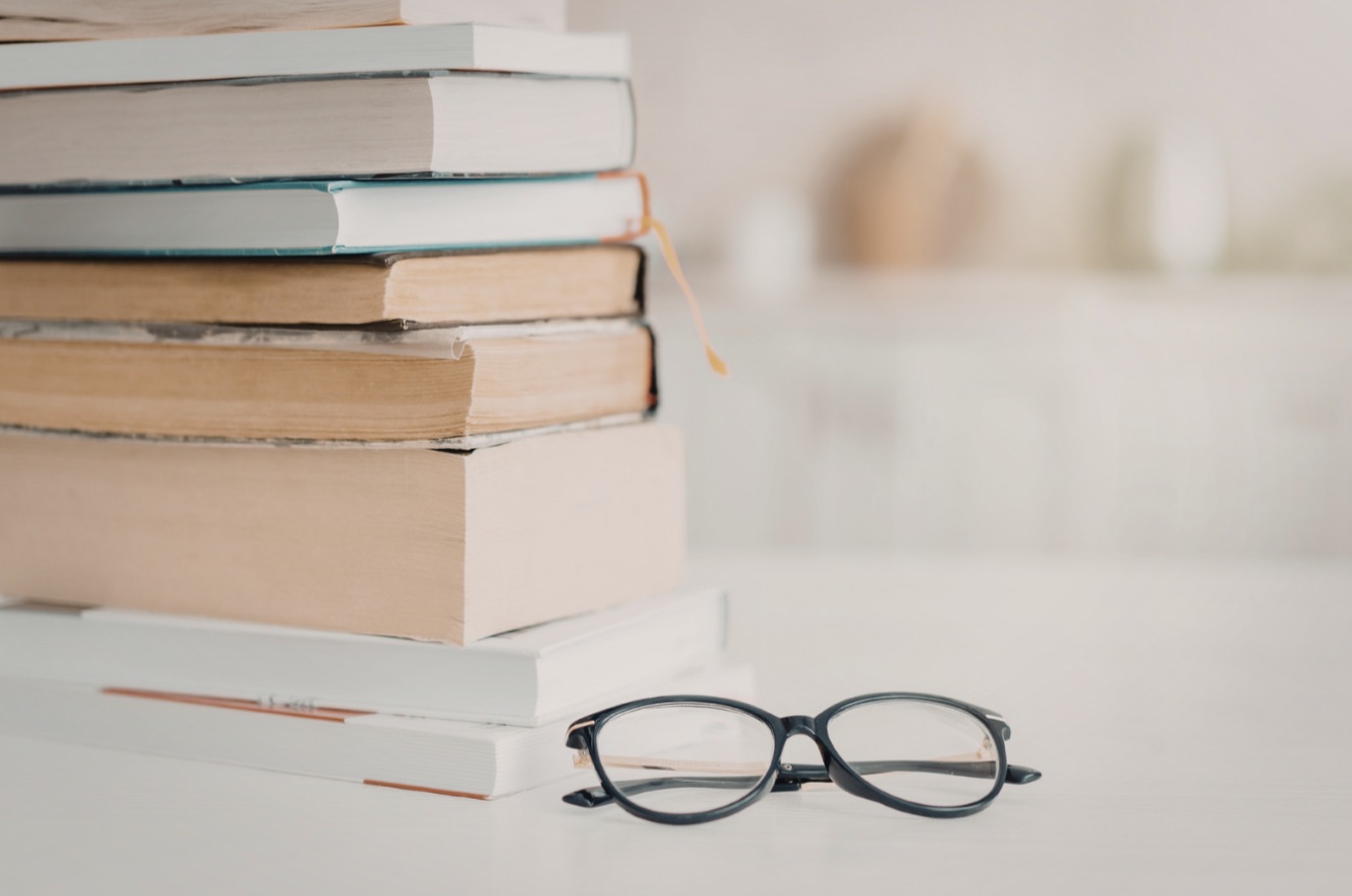 Stack of well-used books with reading glasses, soft natural light