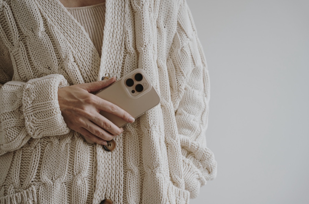 Hands holding a phone in a cream knit cardigan, warm neutral palette