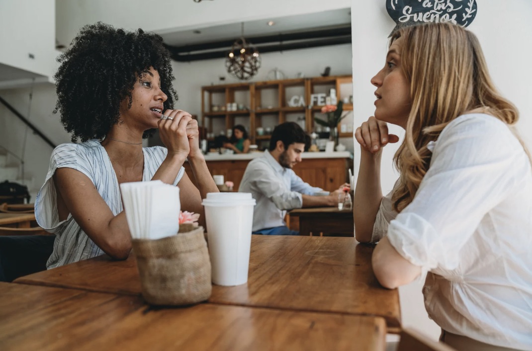 Two women in genuine conversation at a wooden café table, listening attentively